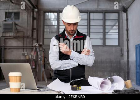 Male engineer thinking while analyzing blueprint on table in building Stock Photo