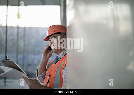 Smiling male architect talking on smart phone at construction site Stock Photo