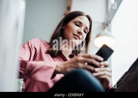 Female freelance worker using mobile phone while sitting in cafe Stock Photo