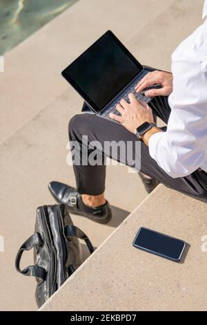 Businessman using digital tablet while sitting on steps during sunny day Stock Photo