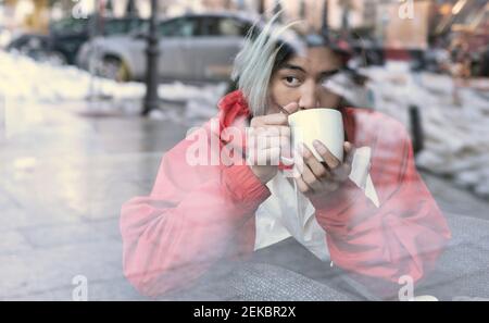 Asian man drinking coffee seen through glass in cafe during winter Stock Photo