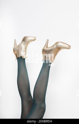 Mature woman wearing golden stilettos against white background Stock Photo