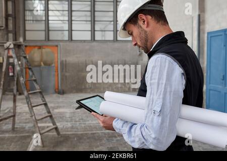Male architect with blueprints using digital tablet while standing in building Stock Photo