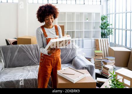Smiling young woman looking at picture frame while unpacking in new apartment Stock Photo