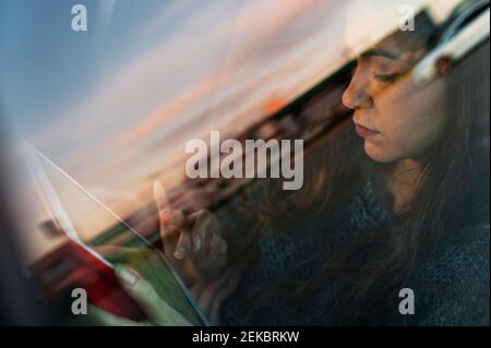 Young woman using digital tablet while travelling in car seen through glass window Stock Photo