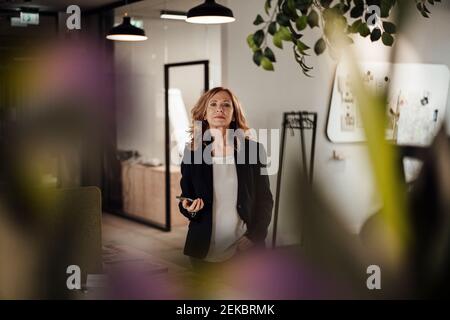 Confident businesswoman with smart phone standing in creative office Stock Photo
