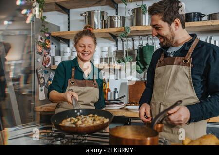 Young chef learning stirring food in pan while standing by colleague in kitchen Stock Photo