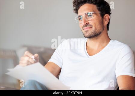 Thoughtful man with paper looking away while sitting at home Stock Photo