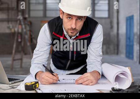 Confident male architect writing on blueprint in building Stock Photo