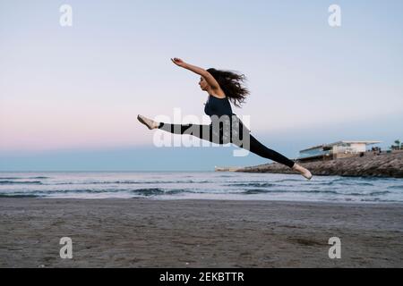 Graceful female ballet dancer with legs apart practicing at beach during sunset Stock Photo