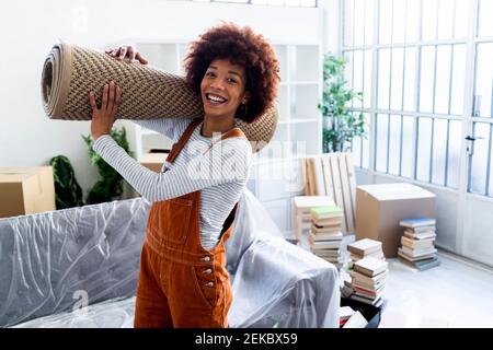 Happy Afro woman carrying carpet while moving in new home Stock Photo