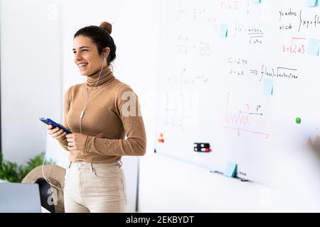Happy female student wearing earphones talking on smart phone at home Stock Photo