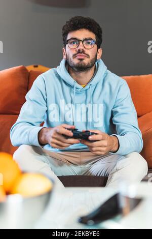 Concentrated young man playing video game in living room Stock Photo