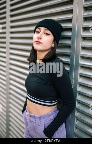 Fashionable young woman with hands in pockets leaning against metallic shutter Stock Photo