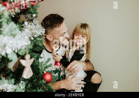 Smiling father holding daughter's hand by Christmas Tree at home Stock Photo
