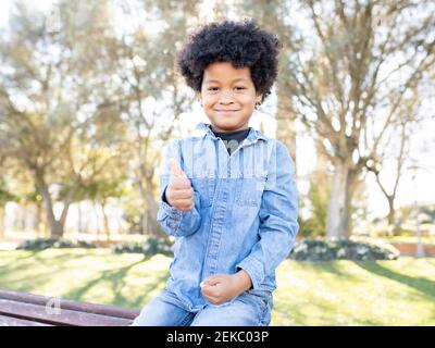 Smiling boy showing thumbs up while sitting at park Stock Photo