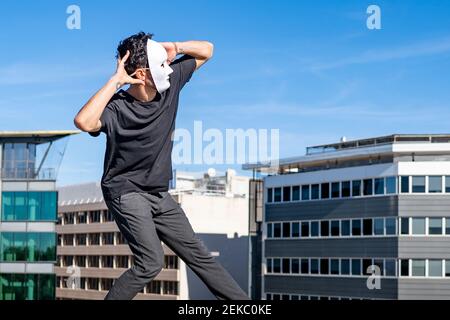 Carefree man with hands behind head dancing while standing on rooftop Stock Photo