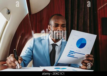Smiling businessman analyzing graph in private jet Stock Photo