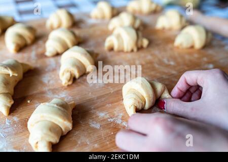 Woman shaping croissants on wooden cutting board in kitchen Stock Photo