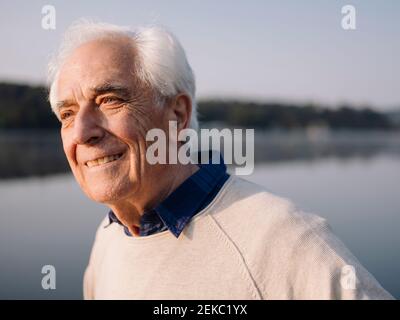 Smiling man looking away while standing against lake Stock Photo