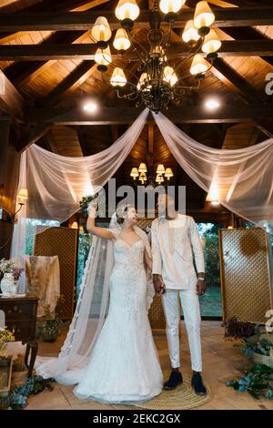 Smiling woman with bouquet holding hand on man while standing at banquet Stock Photo