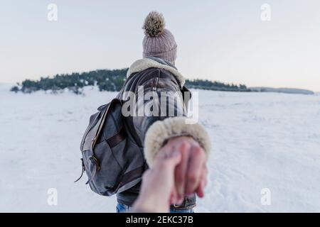 Male backpacker holding woman's hand while walking on snow during sunset Stock Photo