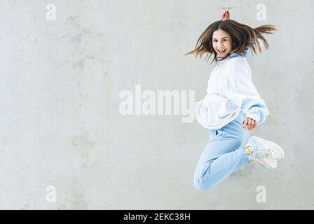 Happy woman smiling while jumping against gray wall Stock Photo