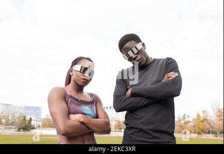 Young male and female sportsperson wearing sunglasses with arms crossed against clear sky Stock Photo