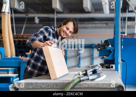Smiling manual worker measuring wood while standing at industry Stock Photo