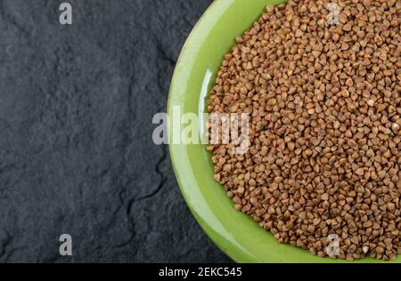 Bunch of raw buckwheat in green bowl Stock Photo