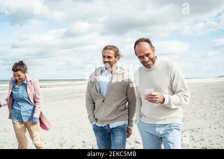 Two men walking and talking side by side along sandy beach Stock Photo