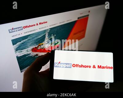 Person holding cellphone with business logo of Singaporean company Keppel Offshore and Marine on screen in front of website. Focus on phone display. Stock Photo