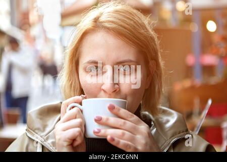 Young European woman drinking coffee in street cafe during cold weather. Stock Photo