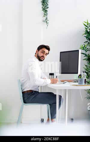 Young businessman with pen sitting in front of computer at work place Stock Photo