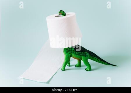 Diplodocus dinosaur toy with a roll of toilet paper around the neck on mint green background Stock Photo