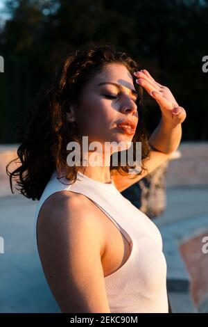 Beautiful woman shielding eyes with hand while standing in park during sunset Stock Photo