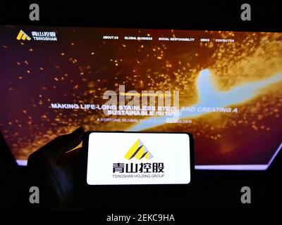 Person holding smartphone with logo of Chinese mining company Tsingshan Holding Group on screen in front of website. Focus on phone display. Stock Photo