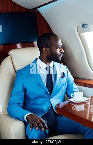 Male entrepreneur looking through window while traveling through airplane Stock Photo