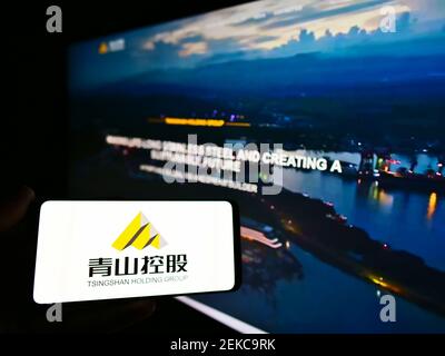 Person holding mobile phone with logo of Chinese steel producer Tsingshan Holding Group on screen in front of webpage. Focus on phone display. Stock Photo