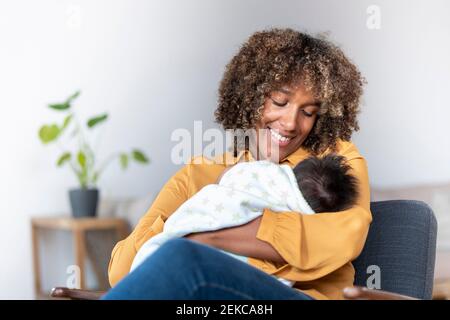 Happy mother looking at baby while sitting on armchair at home Stock Photo