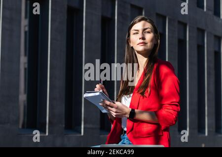 Confident female entrepreneur with diary looking away by structure Stock Photo