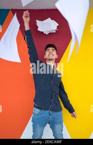Handsome young man holding bunch of papers against multi colored wall Stock Photo