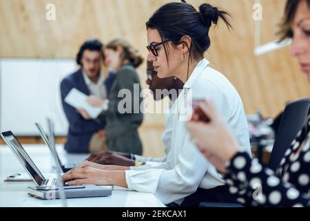 Businesswoman using laptop while sitting amidst colleagues in coworking office Stock Photo