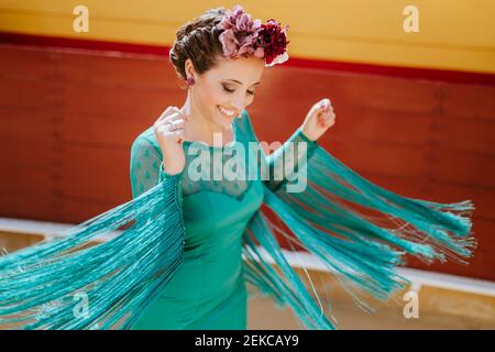 Smiling young woman wearing blue dress and flowers dancing in bullring Stock Photo