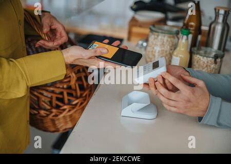 Store clerk holding bar code scanner for female customer while making contactless payment in retail store Stock Photo