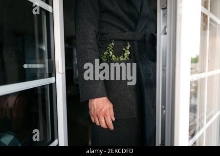 Mature man in black coat with plant in pocket standing at doorway Stock Photo