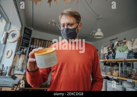 Mature man checking label on food container in zero waste shop during pandemic Stock Photo