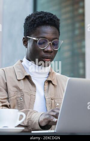 Young man in eyeglasses using laptop at sidewalk cafe Stock Photo