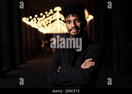 Young man smiling while standing with arms crossed at corridor Stock Photo