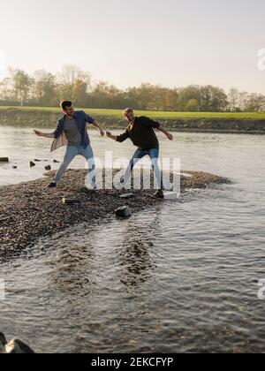 Father and son throwing pebbles in river during autumn Stock Photo
